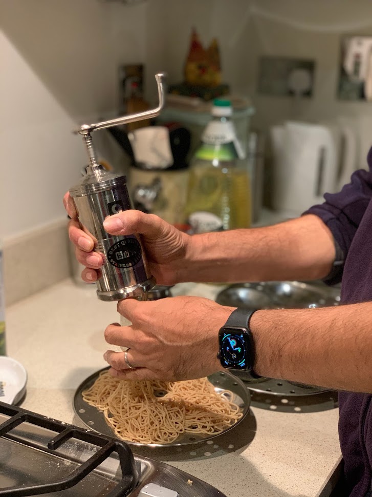 You can see a man's hands holding an Indian device to make string hoppers and in the back are various things - slightly blurred images of a bottle of oil and egg holder